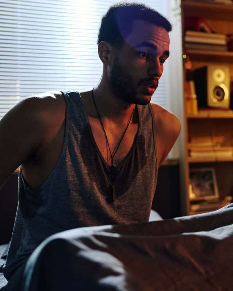 Young scared man sitting on bed after nightmare<br />

