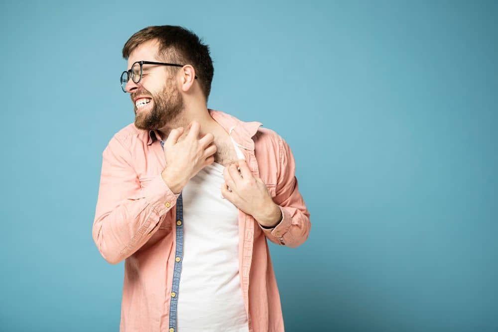 man in glasses scratches itchy skin on neck with hand