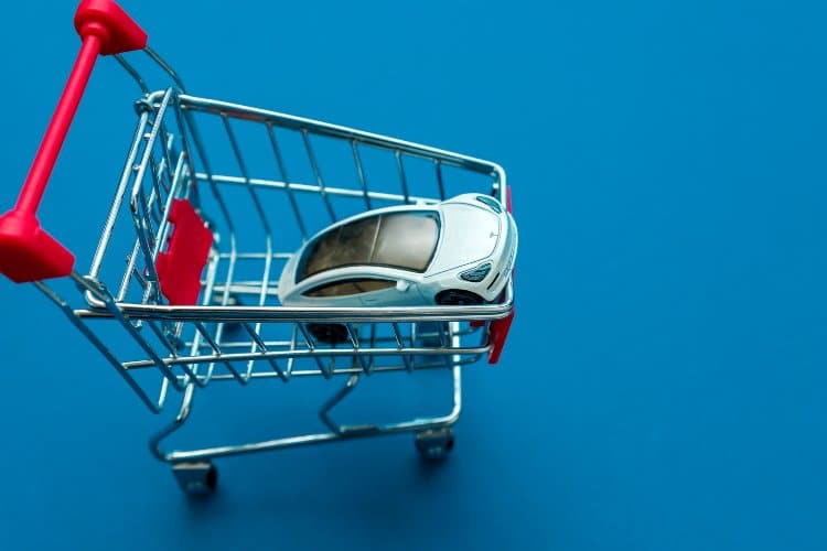 Tesla toy model car in small shopping cart on blue background. 